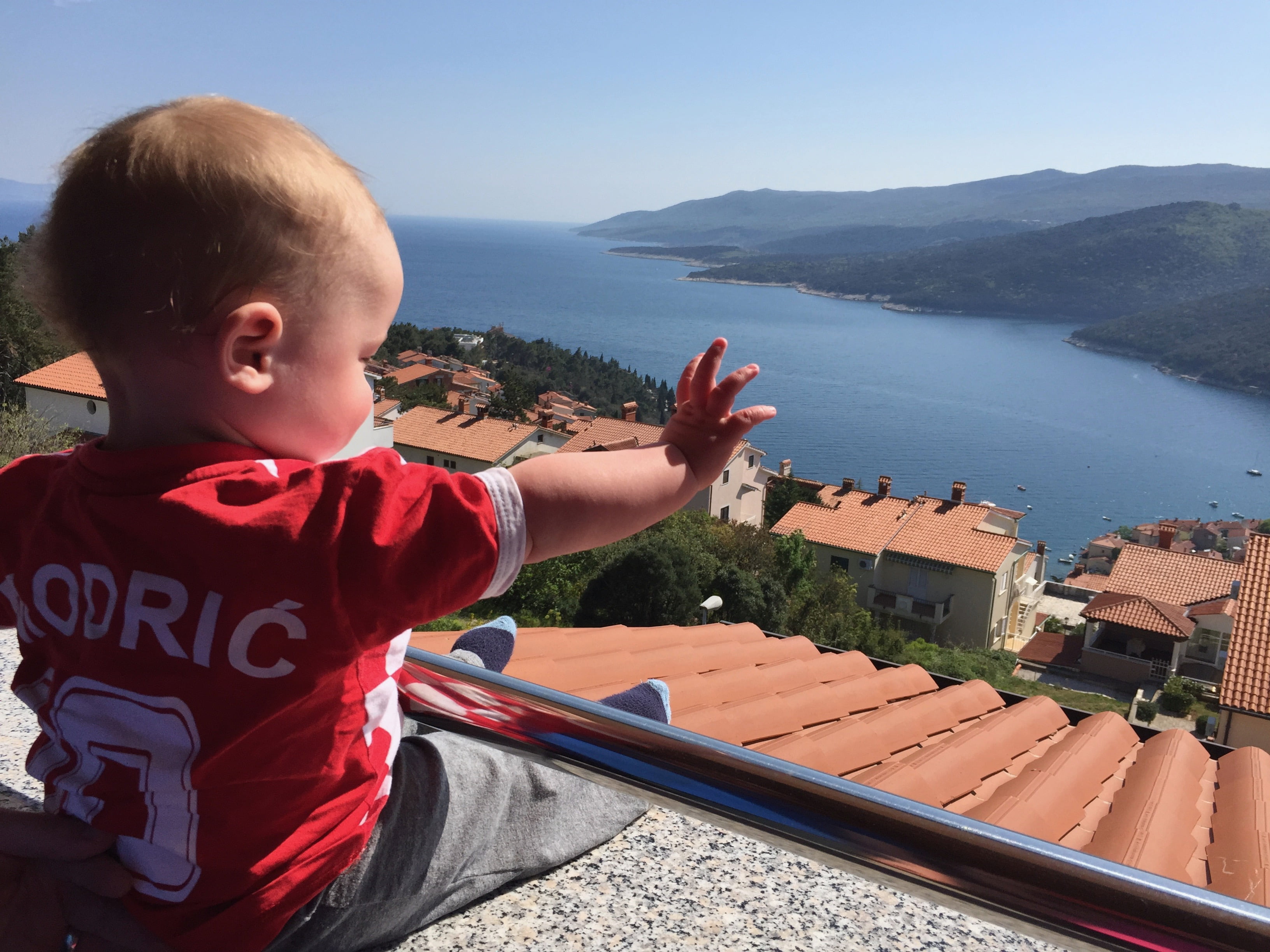 Baby Wearing Croatia Soccer Jersey Waving at View of Ocean